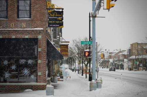 Snow-covered street scene featuring a restaurant sign and traffic light, with buildings and snowflakes in the windows.