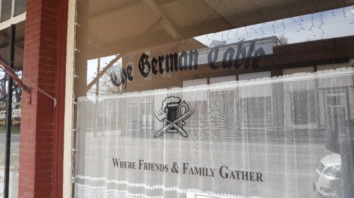 Sign for "The German Table" featuring a beer mug and utensils, with the tagline "Where Friends & Family Gather."