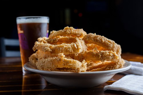 A plate of crispy fried onion rings next to a glass of beer on a wooden table.