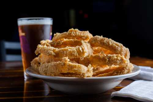 A plate of crispy fried onion rings next to a glass of beer on a wooden table.