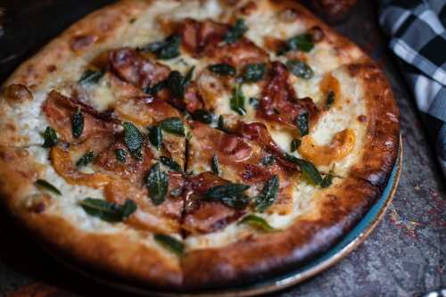 A close-up of a pizza topped with bacon, sage, and melted cheese on a golden crust.