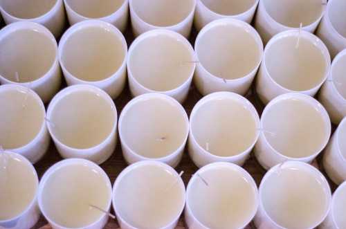 A top-down view of numerous white candle containers filled with wax, each with a wick in the center.