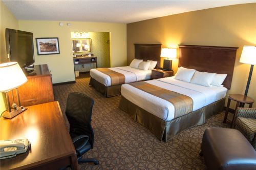 A hotel room featuring two beds, a desk, a chair, and a TV, with warm lighting and a cozy atmosphere.