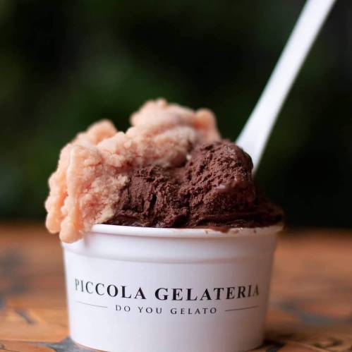 A cup of gelato featuring chocolate and peach flavors, with a spoon, on a wooden surface.