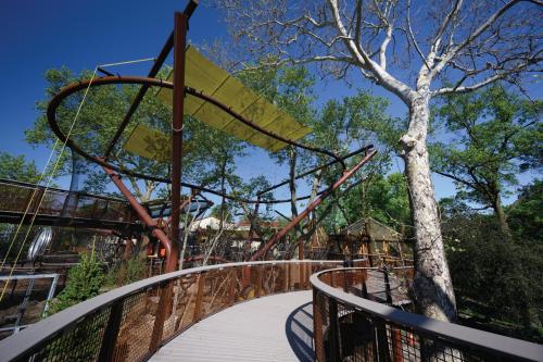 A modern playground structure with curved metal beams, surrounded by trees and a clear blue sky.