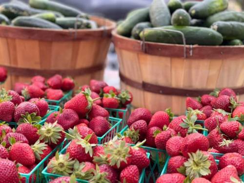 Baskets of fresh strawberries and cucumbers at a market, showcasing vibrant red and green produce.