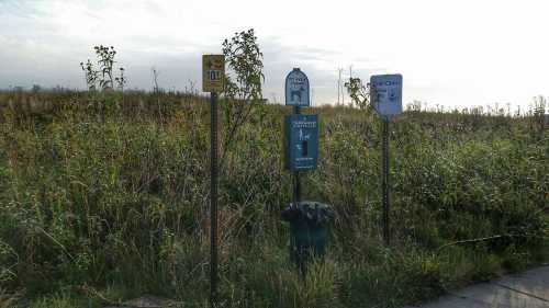 A grassy area with several signs, including bus stops and a notice, under a cloudy sky.