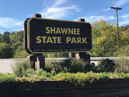 Sign for Shawnee State Park, featuring the park's name and department of conservation details, surrounded by greenery.