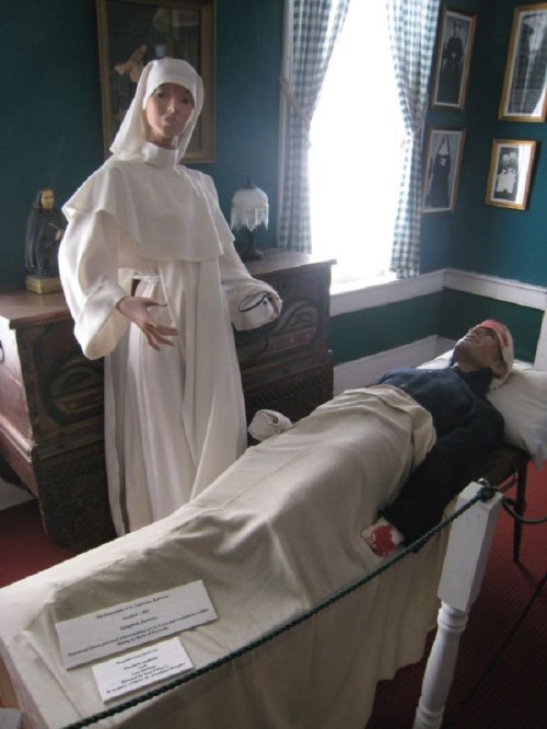 A historical display featuring a mannequin in a nun's habit beside a bandaged figure on a bed.