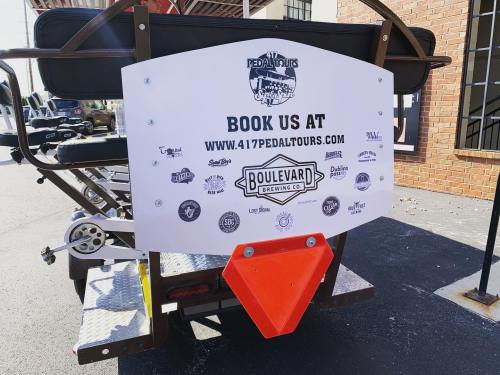 Sign on a pedal tour vehicle promoting bookings at 417pedaltours.com, featuring various logos and a brewery partnership.