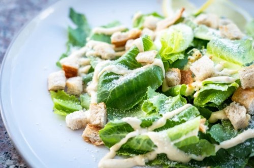 A fresh salad with romaine lettuce, croutons, and creamy dressing on a white plate.