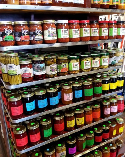 A colorful display of various jars filled with sauces, pickles, and preserves on metal shelves.