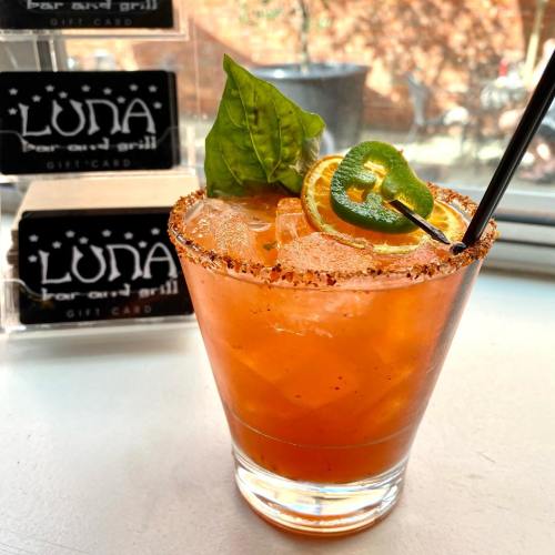 A refreshing cocktail garnished with a lime slice and basil, served in a glass with a salted rim.
