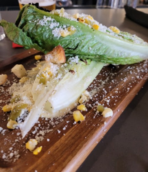 Grilled romaine lettuce topped with cheese, corn, and croutons on a wooden serving board.