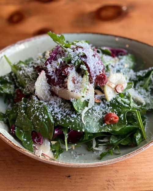 A fresh salad with mixed greens, sliced almonds, cranberries, and grated cheese in a rustic bowl.