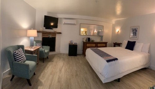 A cozy hotel room featuring a bed, seating area, TV, and a small kitchenette with modern decor.