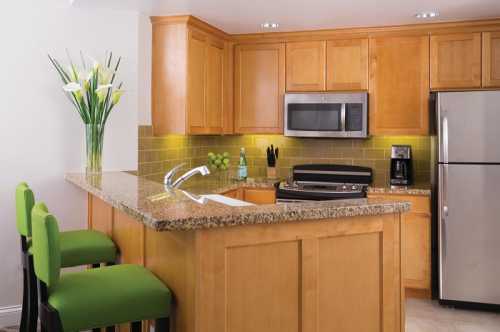 Modern kitchen with wooden cabinets, granite countertop, stainless steel appliances, and green bar stools.