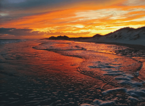 A vibrant sunset over a beach, with waves gently lapping at the shore and colorful clouds in the sky.