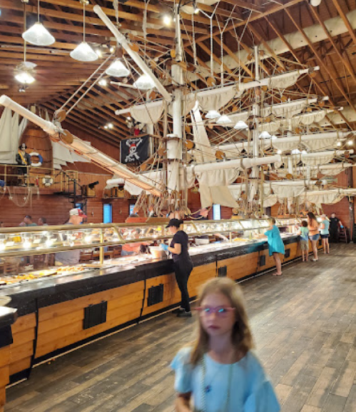 A bustling buffet in a pirate-themed restaurant with ship decor and guests enjoying food.