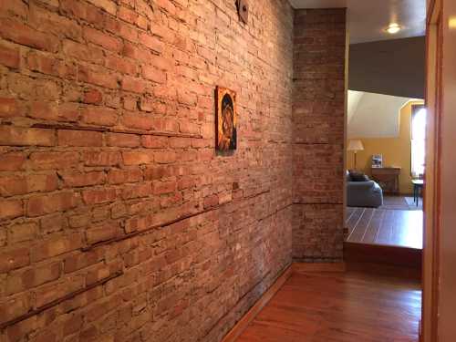 A hallway with exposed brick walls, featuring a small artwork and leading to a cozy living area.