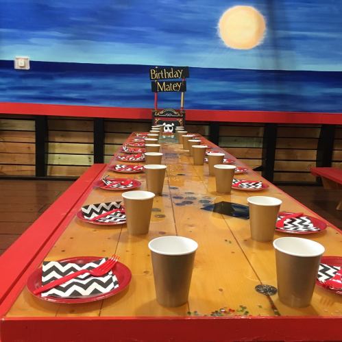 A festive birthday table setting with red and black plates, cups, and a "Birthday Matey" sign against a blue backdrop.