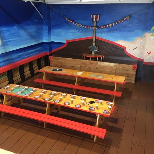 Colorful pirate-themed room with wooden benches and tables, decorated with a mural of the sea and a ship.