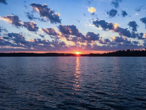 A serene sunset over a calm lake, with colorful clouds reflecting on the water's surface.
