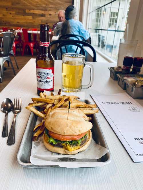 A burger with cheese and tomato, fries, a beer, and a Budweiser on a tray at a restaurant table.