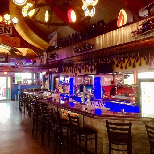 A vibrant bar interior with colorful decor, neon lights, and a long counter lined with chairs.