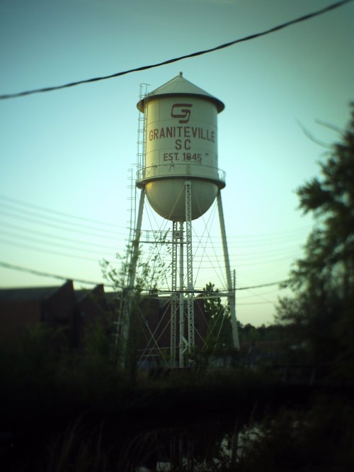 Water tower in Graniteville, SC, established in 1845, surrounded by trees and power lines.