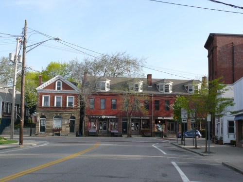 A quaint street scene featuring historic buildings, trees, and power lines under a clear blue sky.