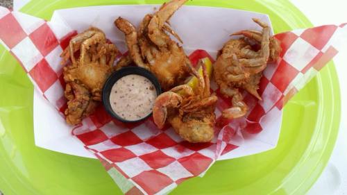 Fried crab claws on a green plate with red and white checkered paper and a side of dipping sauce.
