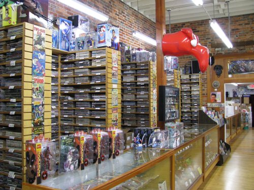 A vibrant comic book store with shelves of comics, collectibles, and a large red inflatable figure hanging from the ceiling.