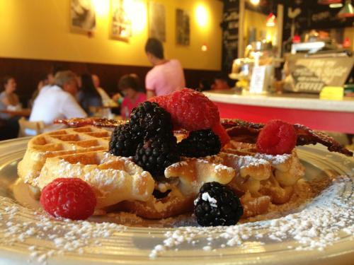 A plate of waffles topped with fresh berries and bacon, dusted with powdered sugar, in a cozy café setting.
