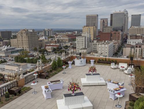 Rooftop event space with white furniture, floral arrangements, and a city skyline in the background under a cloudy sky.