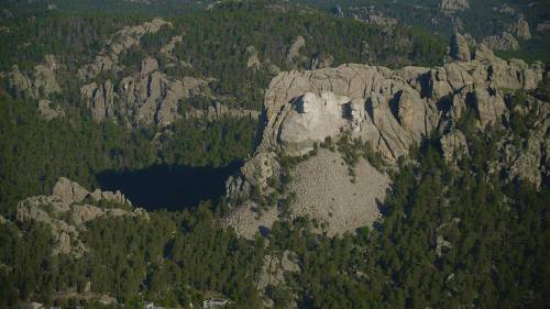 Aerial view of rugged rock formations and dense forest, with a dark lake nestled among the landscape.