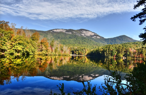 A serene lake reflects a mountain landscape, surrounded by colorful autumn foliage under a clear blue sky.