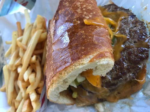 A juicy cheeseburger in a toasted bun, topped with melted cheese and pickles, served with a side of crispy fries.