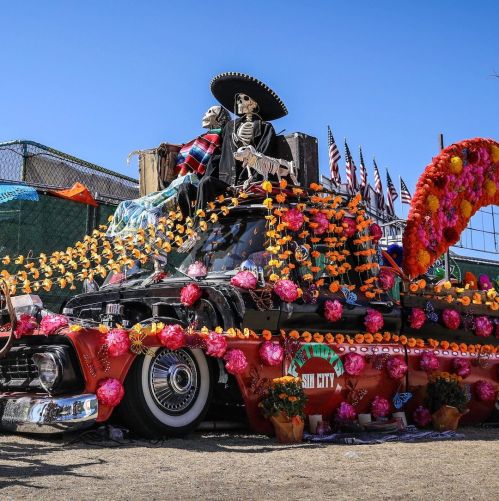 A decorated truck with skeletons, flowers, and vibrant colors, celebrating Día de los Muertos.