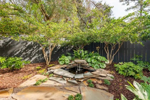 A serene garden scene featuring a small stone fountain surrounded by lush greenery and trees.