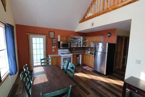 Cozy kitchen and dining area with wooden table, green chairs, and modern appliances in a bright, open space.