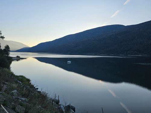 A serene lake at dawn, surrounded by mountains, with a small boat gently floating on the calm water.