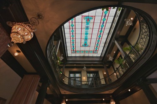 View of an ornate interior with a stained glass ceiling and decorative chandelier, showcasing elegant architectural details.