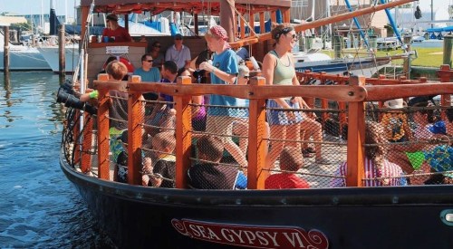 A group of children and adults on a wooden boat, enjoying a day on the water at a marina.