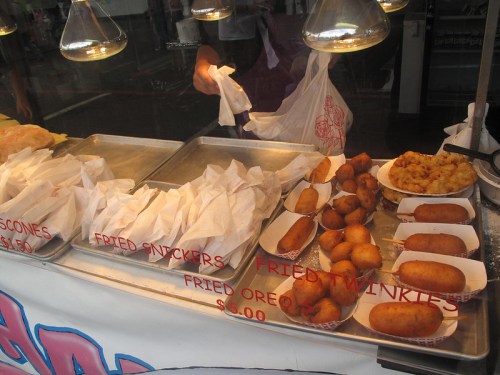 A food stand displaying various fried snacks, including fried Snickers, Twinkies, Oreos, and corn dogs, with prices listed.