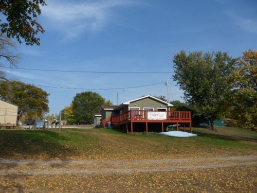 A gray house with a red deck, surrounded by trees and a grassy area, under a clear blue sky.