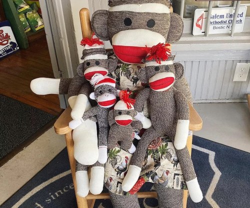 A collection of sock monkeys of various sizes sitting together on a chair, with a floral-patterned cushion.