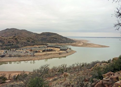 A serene landscape featuring a calm lake surrounded by hills and a sandy shoreline under a cloudy sky.