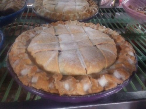 A freshly baked pie with a golden crust and a crisscross pattern on top, displayed on a rack.