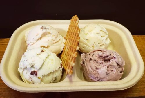 A tray with four scoops of ice cream in different flavors, topped with a waffle cone piece.